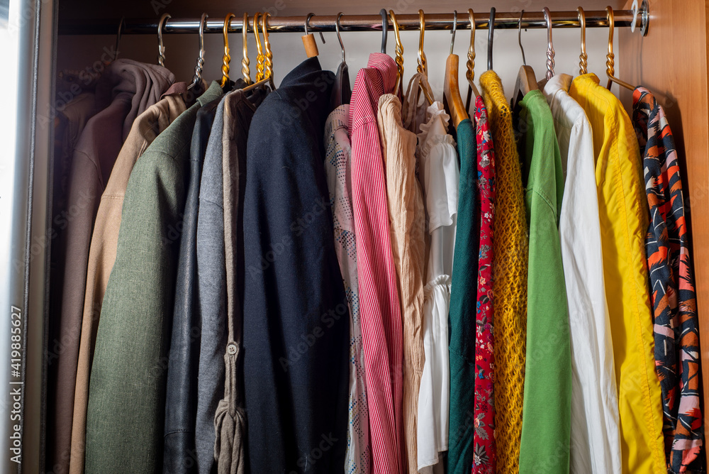 Organizing a variety of clothes in a wardrobe. Clothes on hangers in dark and light colors. Separation of men's and women's wardrobe