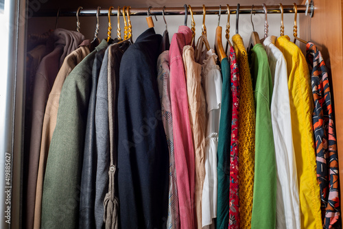 Organizing a variety of clothes in a wardrobe. Clothes on hangers in dark and light colors. Separation of men's and women's wardrobe
