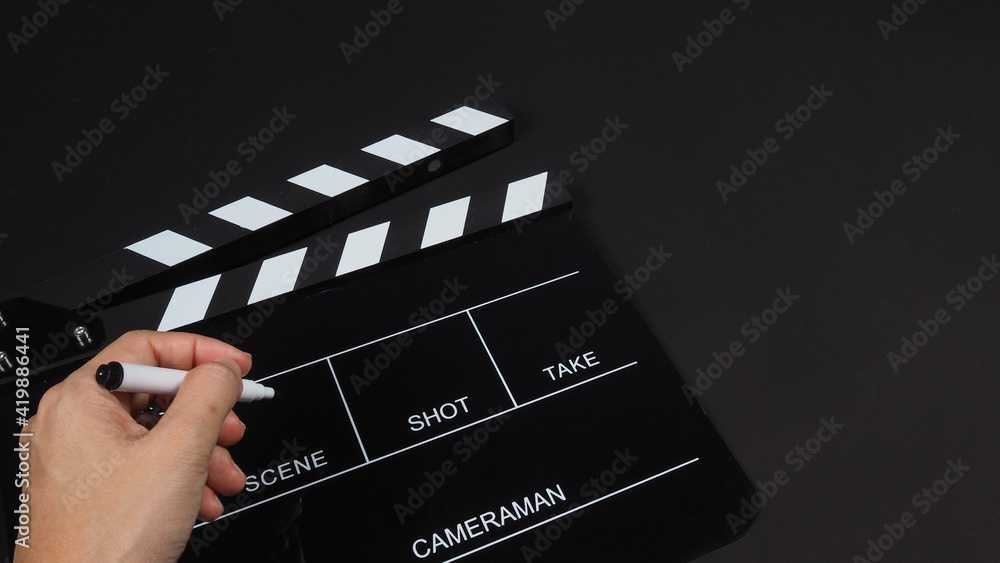 Hand is holding pen and Black Clapperboard or clap board or movie slate use in video production ,film, cinema industry on black background.