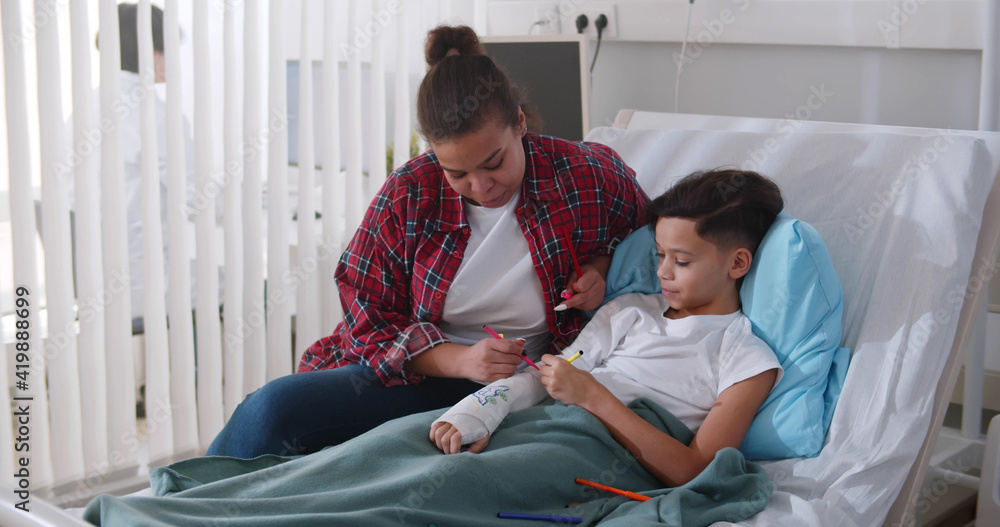 Caring African Mother Visiting Son With Broken Arm In Bed In Hospital