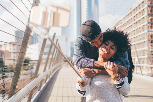 Young black man and woman tourist couple using smartphone taking selfie with selfie stick photo