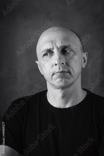 A serious middle-aged man with an unshaven face and a bald head looks thoughtfully to the side. Black and white portrait. Photo taken in studio