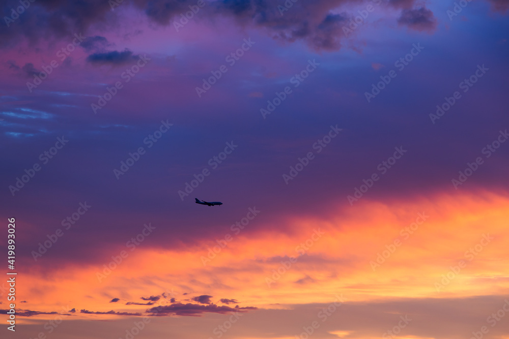 Horizontal view of plane flying above sunset with dramatic coloured sky, Montreal, Quebec, Canada