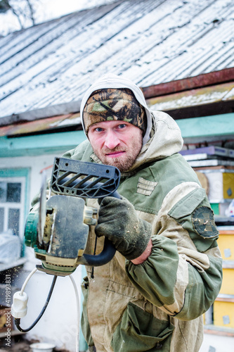 Man angry in military clothes. Work picked up a power saw. Man scares chainsaw an opponent in the street in winter