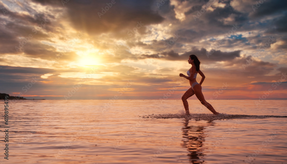 Young beautiful sexy fit lingerie brunette  model running in the water at dramatic sunset 