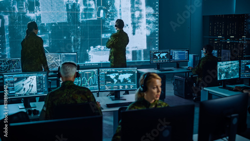 Fotografie Military Surveillance Team of Officers Locked a Target on a Vehicle from a Satellite and Monitor it on a Big Display in Office for Cyber Operations for Managing Security and Army Communications