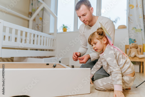 Little 4-years girl helps her father assemble kids bed