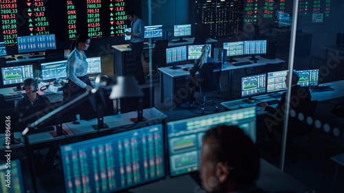 Professional Financial Data Analysts Working in a Modern Monitoring Office with Live Analytics Feed on a Big Digital Screen. Monitoring Room with Finance Specialists Sit in Front of Computers.