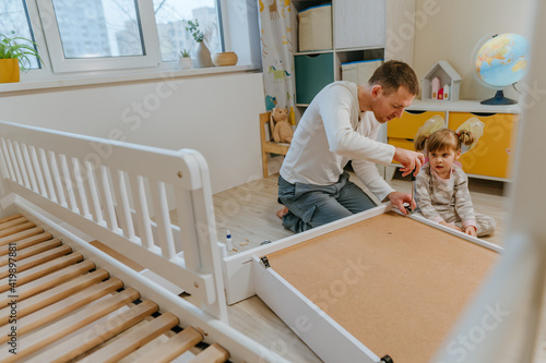 Foto Little 4-years girl helps her father assemble kids bed