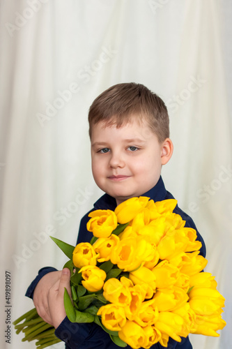 Portrait of a young, beautiful boy. Holds a huge armful of fresh yellow tulips. The concept of spring and holiday, March 8, International Women's Day