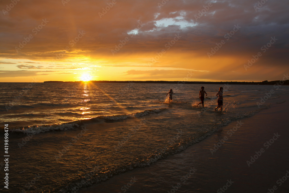 Kids in silhouette running on the beach with a beautiful sunset