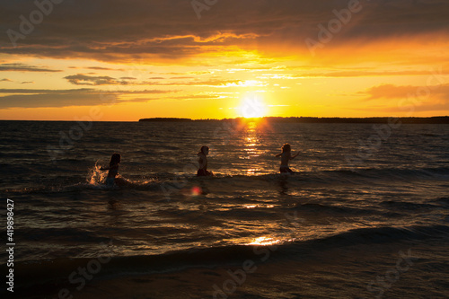 Kids in silhouette playing in the water and a sunset