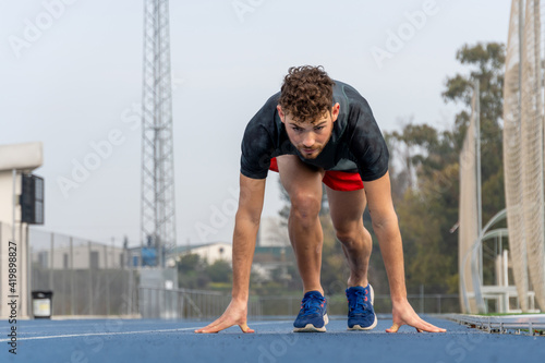 Concentrated athlete in starting position in blue running track.