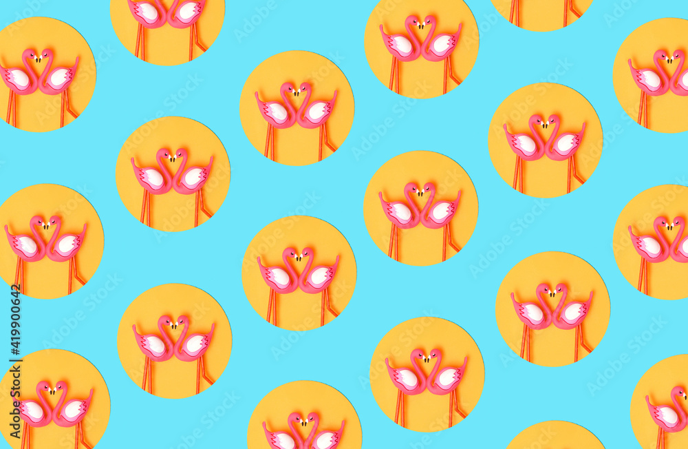 Fototapeta premium Pattern created of two flamingo toys in orange circle on neon blue background. Top view.