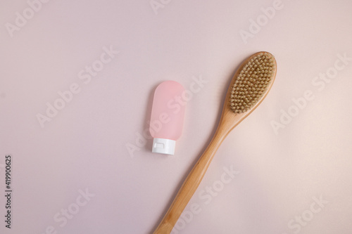 Eco body brush and pink tube with body scrub or cream over pale pink background with copy space.
