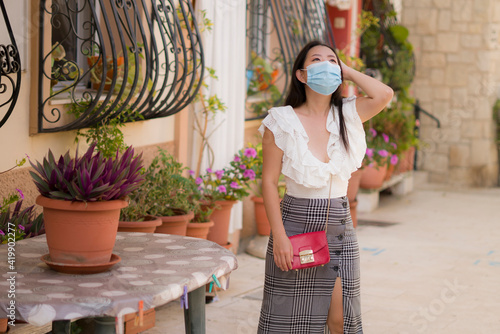 Asian woman touring in Andalusia Spain during covid19 - young happy and beautiful Japanese girl in face mask enjoying holidays travel walking traditional street in Seville town