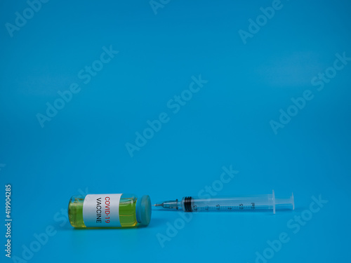 An image of a vial covid-19 vaccine and syringe isolated on a blue background. Healthcare and medical concept. Selective focus image.