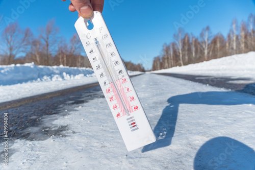 Фотография The thermometer shows a negative temperature in cold weather against the background of an icy road or highway