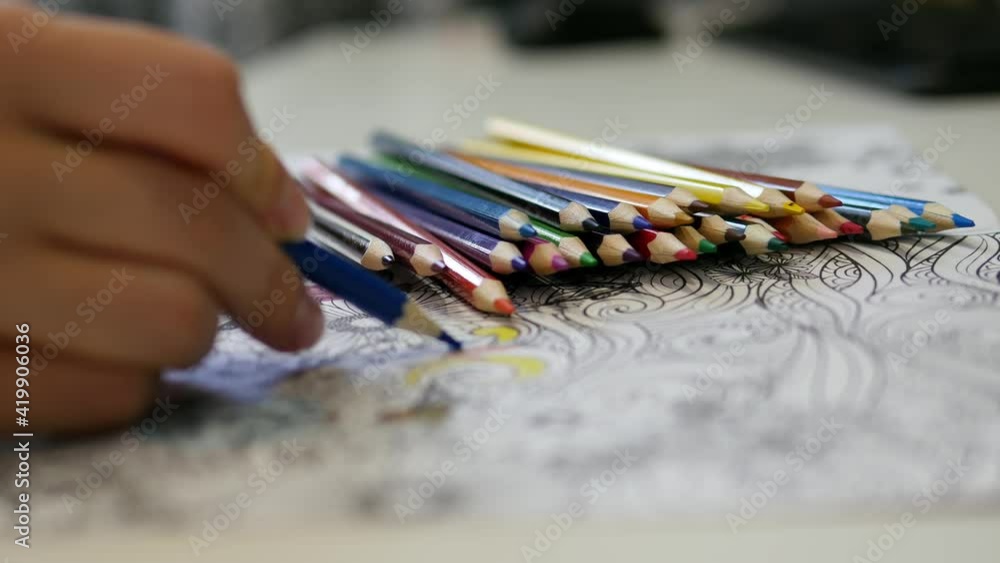 Close-up of a girl's hand paints an antistress coloring book. Calming the nerves with color therapy. Close-up of a girl's hand paints an antistress coloring book. Calming the nerves with color therapy.