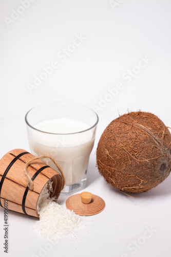 fresh coconut near wooden bowl with coconut flakes and glass of coco milk. isolated on white background. tropical nut