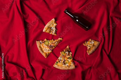 Top view - Leftovers slices pizza with bottle beer in red textile background. After party concept. 