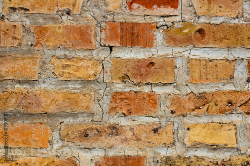 Symmetrical brick wall background. Red and brown colored terracotta bricks from an abandoned house  some clean  some dirty. Cracks in the wall.