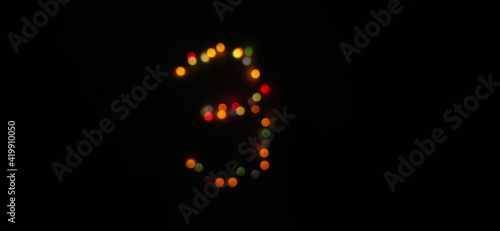 Closeup of Number three (3) made with multicolored blurred bokeh Christmas lights in a isolated black background with a selective focus on number and Copy space