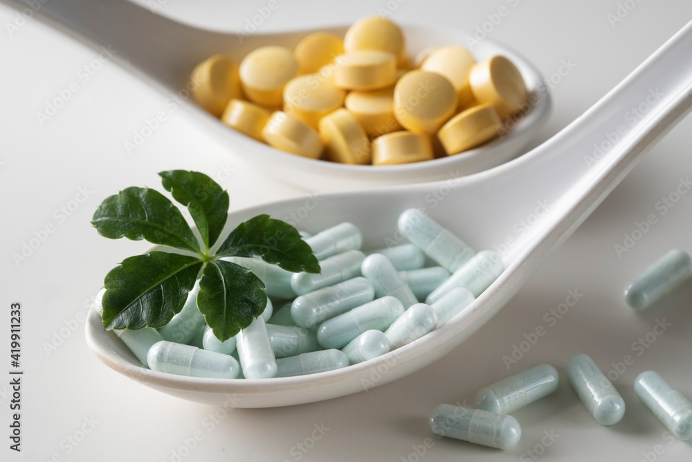 Spoons filled with different tablets with green leaf on a white background. As a concept of natural medicines. Spoons filled with different tablets with green leaf on a white background. As a concept of natural medicines.