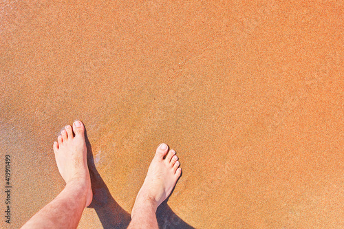 Closeup of man's bare feet stand at wet on beach. Vacation on ocean beach, foot on sea sand. Empty copy space. Summer atmosphere.