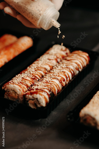 The chef sprinkles sesame seeds on a take-away sushi set
