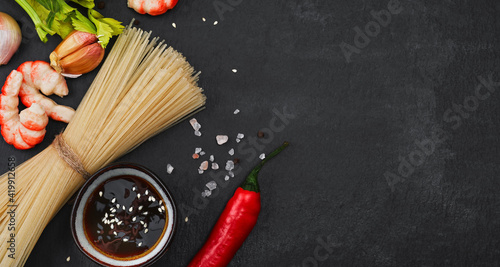 Layout of ingredients for making fried noodles with shrimp, seafood, soy sauce and spices are placed on a black stone background. Top view, flat minimal design, asian food concept