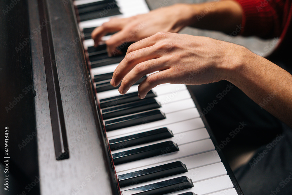 Close-up hands of unrecognizable man playing on piano at home recording studio. Closeup side view fingers of male playing digital electronic piano synthesize. Concept of music education.