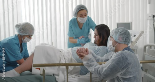 Obstetricians and husband supporting female giving birth in hospital