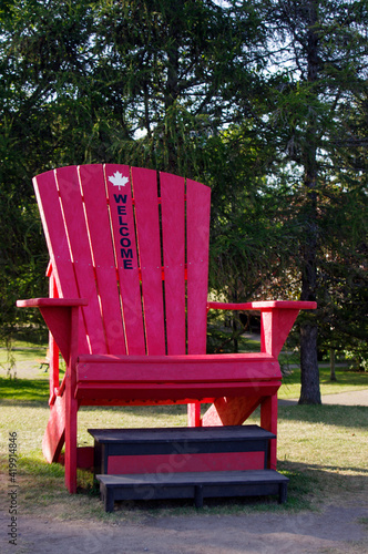 large red Adirondack chair in park¬ with welcome on it