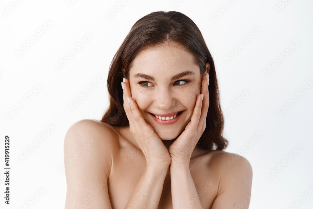 Skincare and beauty. Girl with nourished and clean skin touching her clean hydrated face, smiling and looking away. Woman with naked shoulders using skin care cosmetics, white background Skincare and beauty. Girl with nourished and clean skin touching her clean hydrated face, smiling and looking away. Woman with naked shoulders using skin care cosmetics, white background