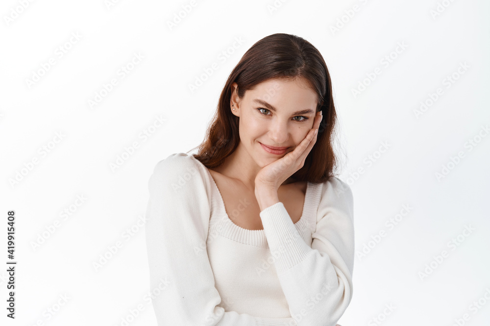 Portrait of cute female model in light blouse, giggle and looking shy, blushing from compliment, smiling at camera modest, standing against white background Portrait of cute female model in light blouse, giggle and looking shy, blushing from compliment, smiling at camera modest, standing against white background