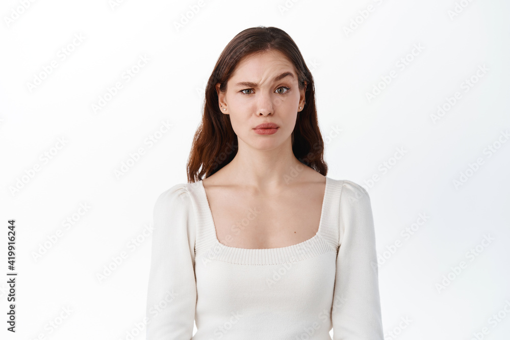 Confused young woman model raising eyebrow with disbelief, look doubtful at something strange, feeling unsure, standing against white background Confused young woman model raising eyebrow with disbelief, look doubtful at something strange, feeling unsure, standing against white background