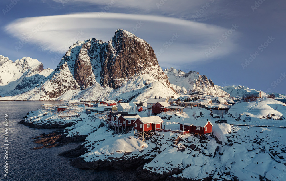 Wonderful wintry landscape. Impressive Winter scenery with Snowcapped mountain, traditional red fishing huts, rorbu and gorgeous sky with fairy tale clouds. Hamnoy village of an ideal resting place.