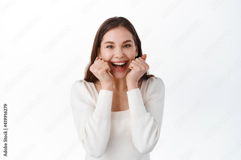 Excited girl screams from happy emotion, winning and rejoicing, staring at camera, achieve goal, celebrate lucky success, gain goal, standing against white background Excited girl screams from happy emotion, winning and rejoicing, staring at camera, achieve goal, celebrate lucky success, gain goal, standing against white background