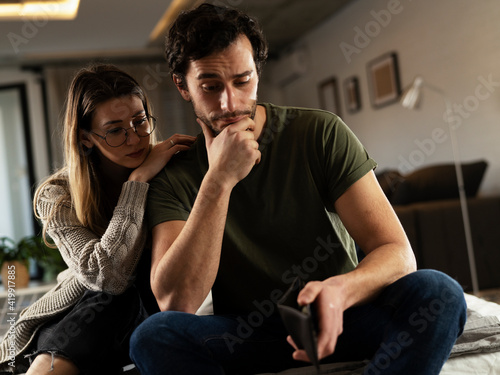Young man checking empty wallet, no money. Unemployed sad man sitting at home with wife showing empty wallet.
