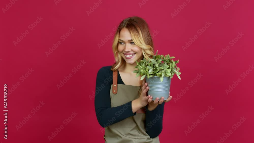 Young blonde girl holding a plant standing and looking to the side over isolated background Young blonde girl holding a plant standing and looking to the side over isolated background