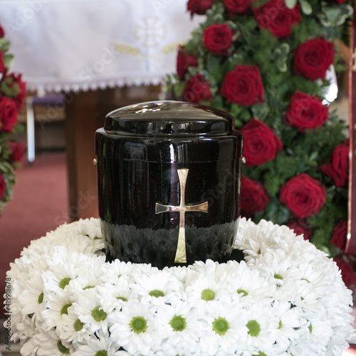 Black urn on the funeral day in church; surrounded with daisies and roses
