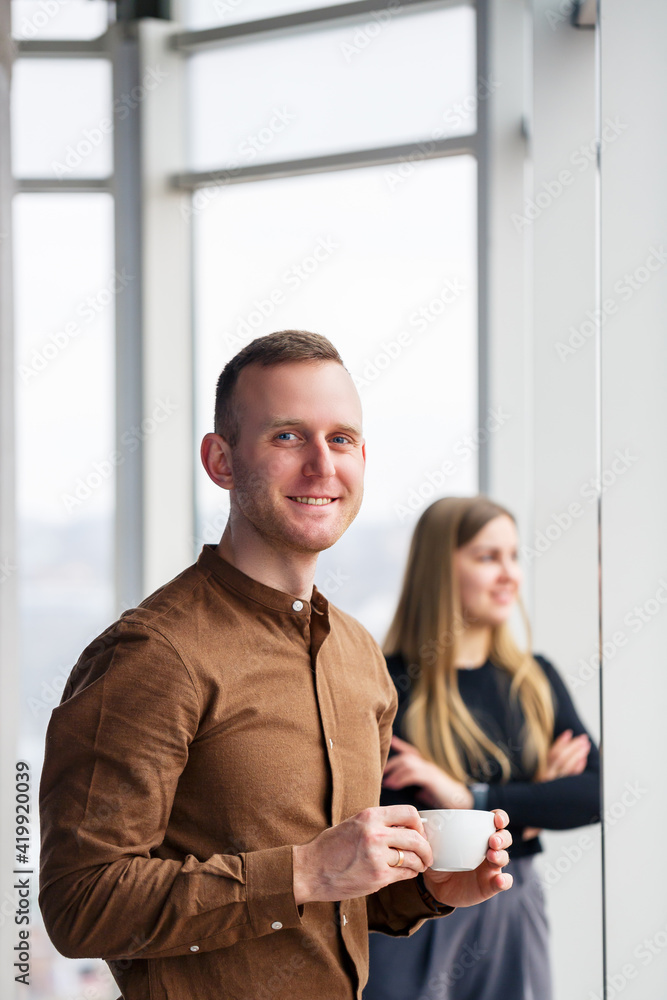 Stylish young couple in love in front of large panoramic windows. A young woman and a man are standing at a large window with coffee. Selective focus Stylish young couple in love in front of large panoramic windows. A young woman and a man are standing at a large window with coffee. Selective focus