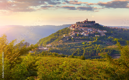Antique city Motovun Croatia Istria. Picturesque panorama age-old village at hill with pink cloud and sunny light and authentic home with red tegular roof and green vineyard garden.
