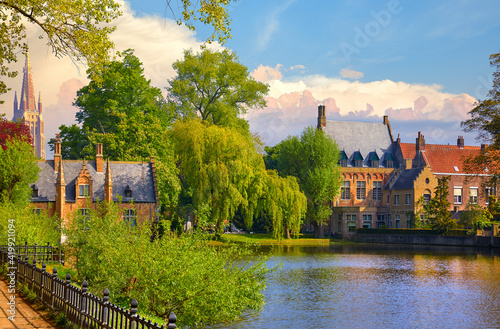 Vintage building over lake of love in Minnewater park in Bruges Belgium near Beguinage monastery of Beguines. Picturesque landscape with green trees sunset time.