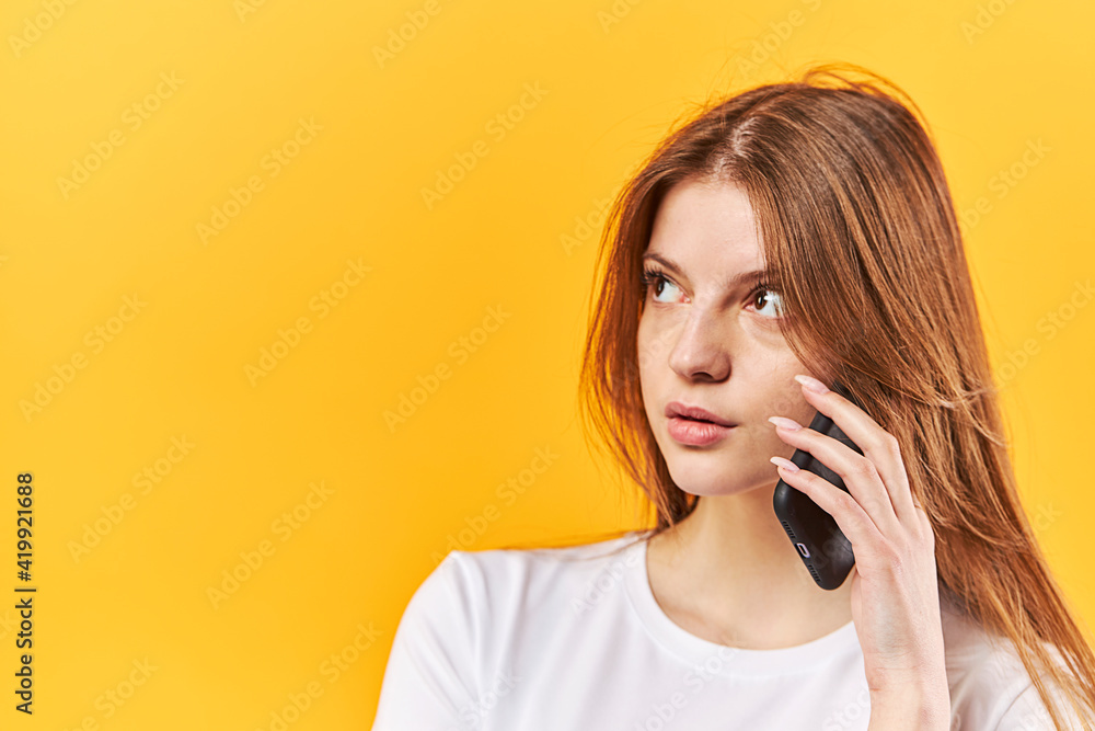 Portrait woman talking on mobile phone and looking away isolated over yellow background Portrait woman talking on mobile phone and looking away isolated over yellow background