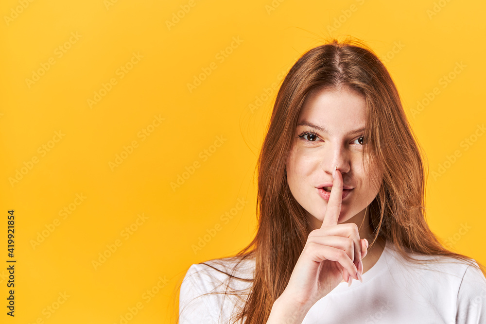 Portrait young girl, showing silence with finger touching lips. Isolated over bright vivid yellow background Portrait young girl, showing silence with finger touching lips. Isolated over bright vivid yellow background