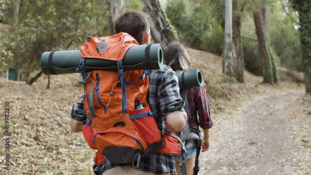 Couple of hikers with camping backpacks walking on forest path, enjoying outdoor vacation, activity and healthy recreation. Dolly shot, back view. Adventure travel concept Couple of hikers with camping backpacks walking on forest path, enjoying outdoor vacation, activity and healthy recreation. Dolly shot, back view. Adventure travel concept