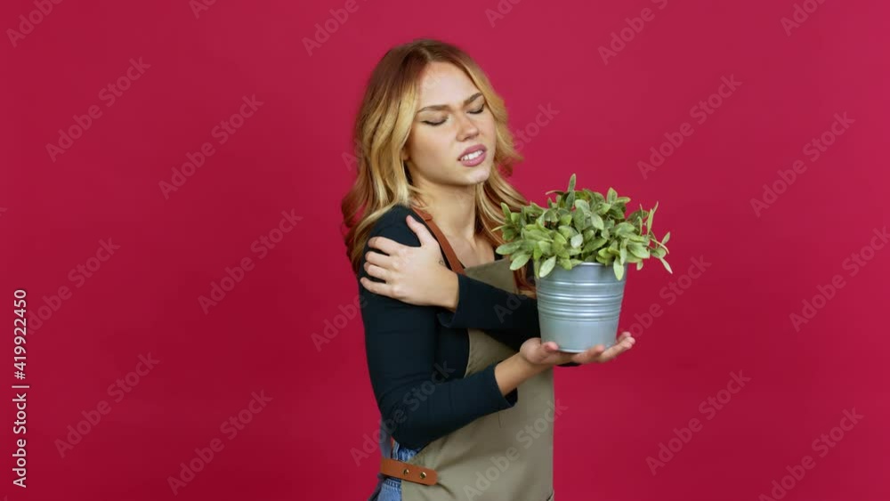 Young blonde girl holding a plant with shoulder pain over isolated background Young blonde girl holding a plant with shoulder pain over isolated background