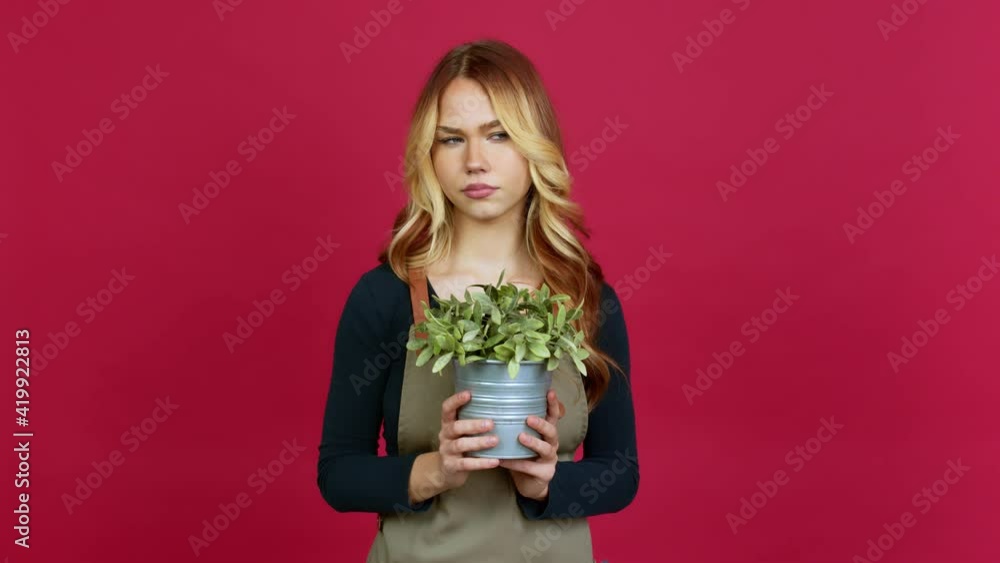 Young blonde girl holding a plant looking side over isolated background Young blonde girl holding a plant looking side over isolated background